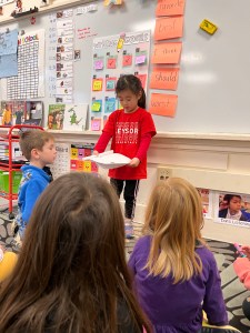 A Kindergarten writer holds up her work in front of the class.