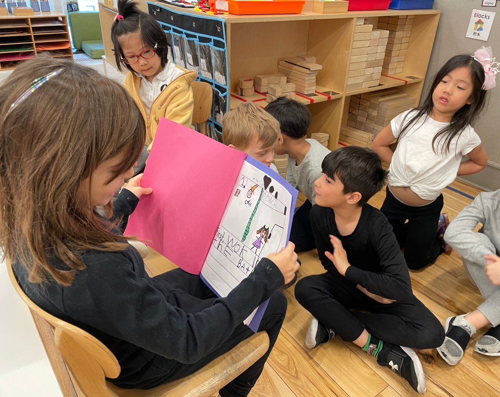 A group of kindergarten students listening to a classmate read her book aloud.