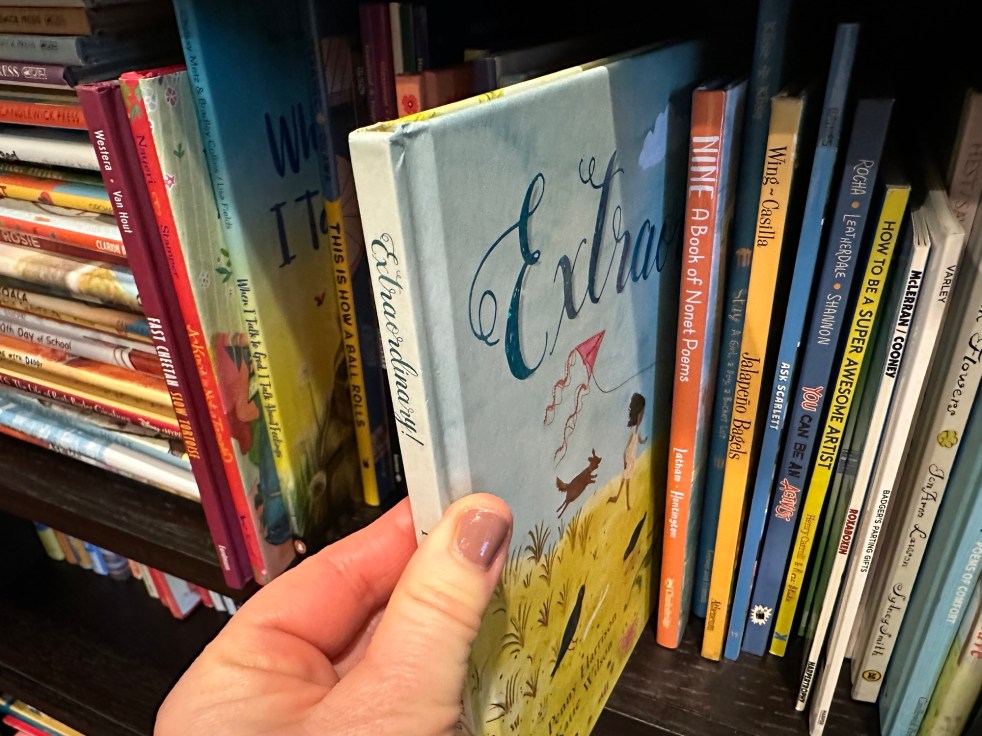 A shelf filled with picture books, with one book being selected by a person's hand.